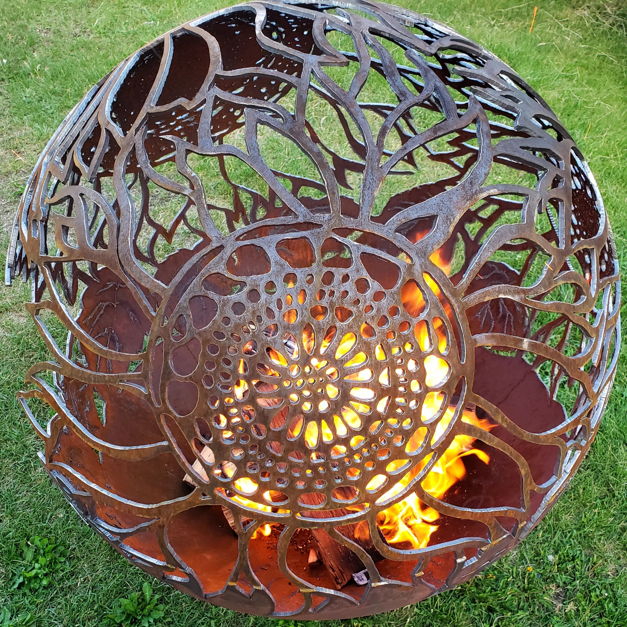 Intricately designed metal fire pit with flames inside on grass.