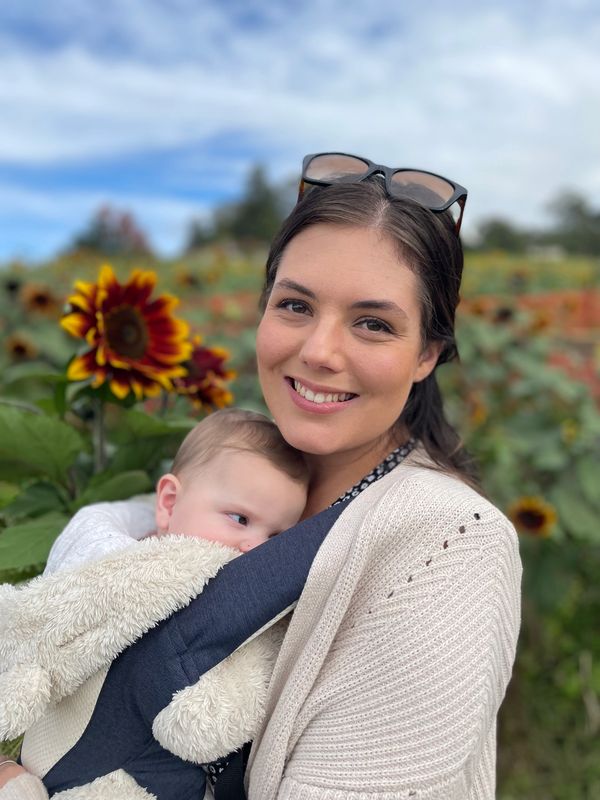 A smiling woman holding a baby in a sunflower field.