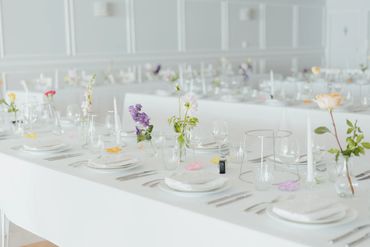 Elegantly set white dining tables with flowers and glassware in a bright room.