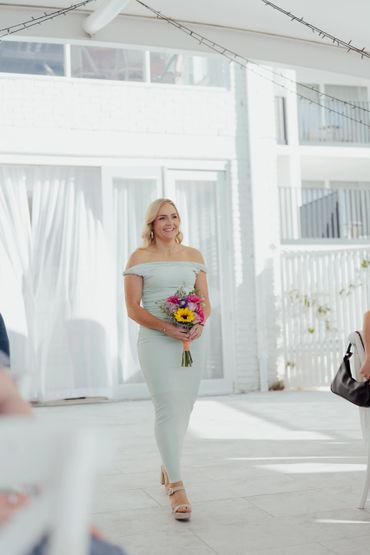 Woman in a light green dress holding a colorful bouquet, smiling indoors.