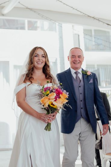 Bride in white dress holding bouquet, smiling beside man in suit.