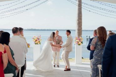 Couple exchanging vows at a waterfront wedding ceremony with guests watching.