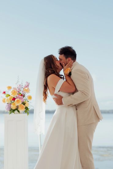 Bride and groom sharing a kiss during a beach wedding ceremony.