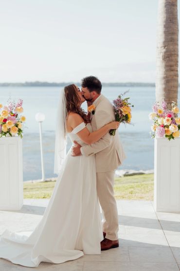 Bride and groom kissing at a waterfront wedding ceremony.