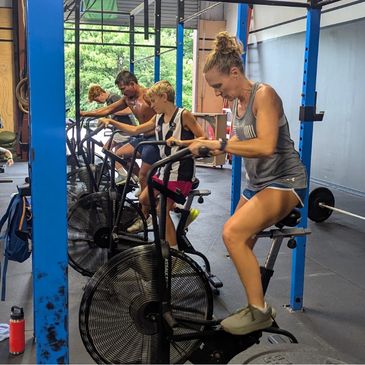 A family of athletes training together on air bikes in a gym.