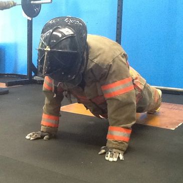 A firefighter in full gear doing push-ups at the gym.