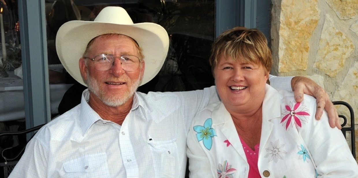 Smiling couple sitting closely, man in white cowboy hat and woman in floral jacket.