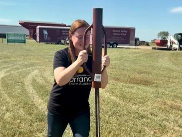 Woman holding a rusty horseshoe stake on a grassy field.