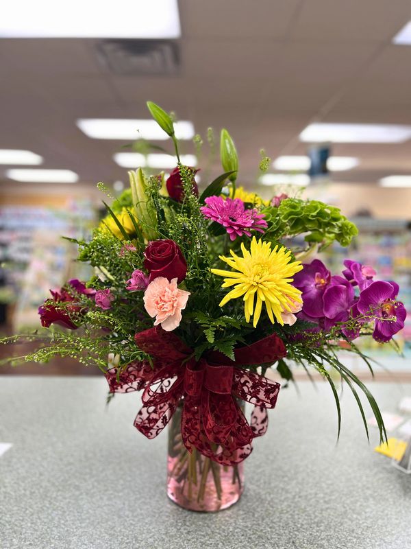 Colorful flower bouquet in a pink vase with a decorative red bow.