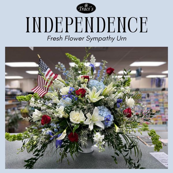Patriotic fresh flower sympathy urn arrangement with red, white, and blue flowers and an American flag.