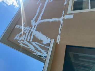 Building exterior with patchy white paint under clear sky.