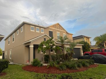 Two-story beige house with palm trees and a red pickup truck.