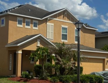Two-story house with beige exterior and plants in front yard.