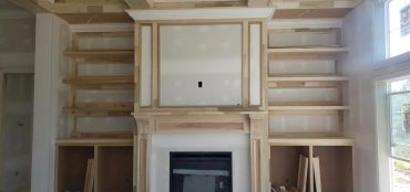 Unfinished wooden fireplace mantel with built-in shelves.