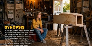 Young girl sitting in a rustic workshop, surrounded by tools and a wooden soap box derby car.