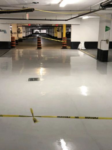 Empty parking garage with caution tape and traffic cones blocking access.