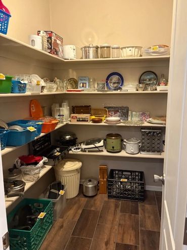 Organized pantry with kitchen appliances, dishes, and storage baskets on shelves.