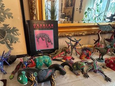 Colorful Oaxaca woodcarvings displayed on a table with a book in the background.