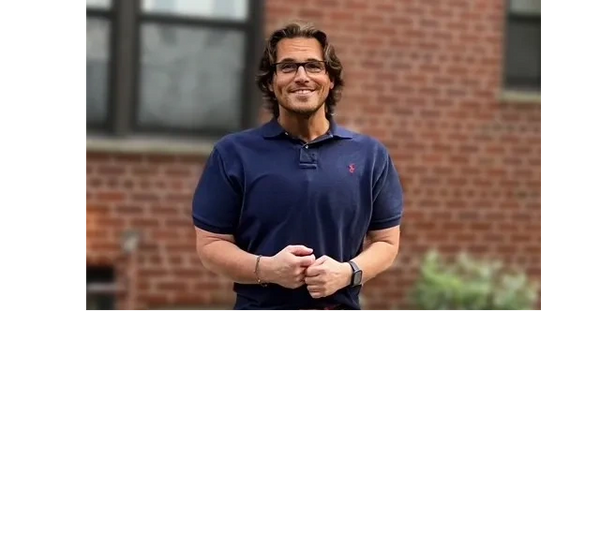 A man in a navy polo shirt smiles while standing outdoors against a brick wall.