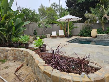 Contemporary pool with large square, stone tiles and traditional stone, retaining wall. Southern Cal