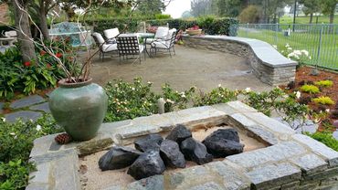 Fire feature with large lava rocks in traditional styled backyard with stone rock wall.