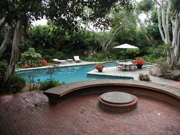 Tropical built-in pool with built-in fire pit and seating area using brick and stone for a tradition