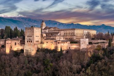 The Alhambra palace against a mountain backdrop at sunset.
