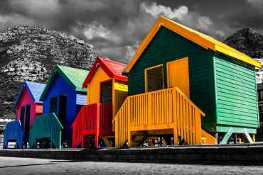 Colorful beach huts stand out against a black and white mountain background.