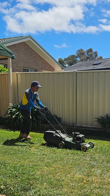 A man mowing the lawn on a sunny day in a backyard.