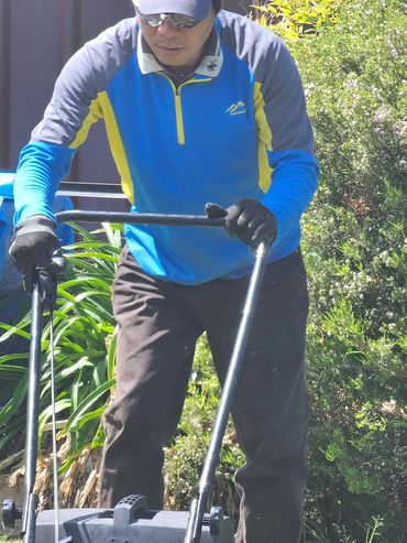Man mowing lawn wearing a blue jacket and cap.