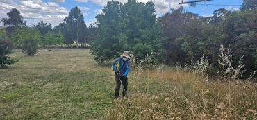 Person wearing a mask and hat using a grass trimmer in a field.