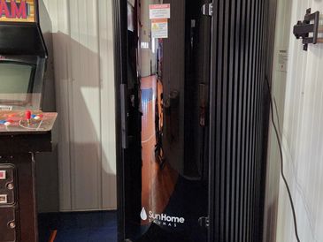 A sleek black SunHome sauna heater in a room corner.