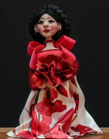 Handcrafted doll with black hair and red floral dress.