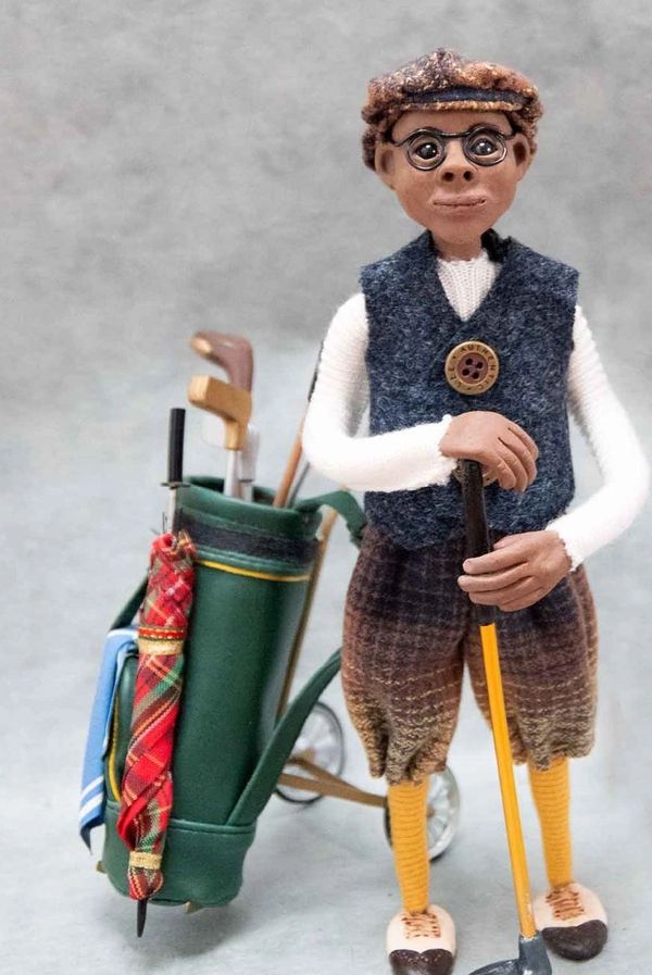 Claymation figure of a golfer with vintage attire and golf bag.