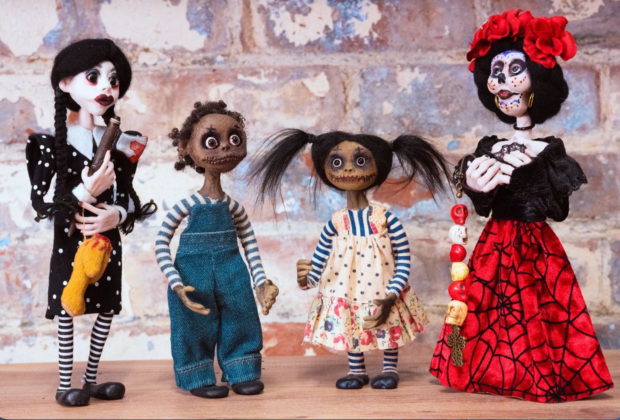 Four spooky dolls with detailed costumes and makeup stand in a row.