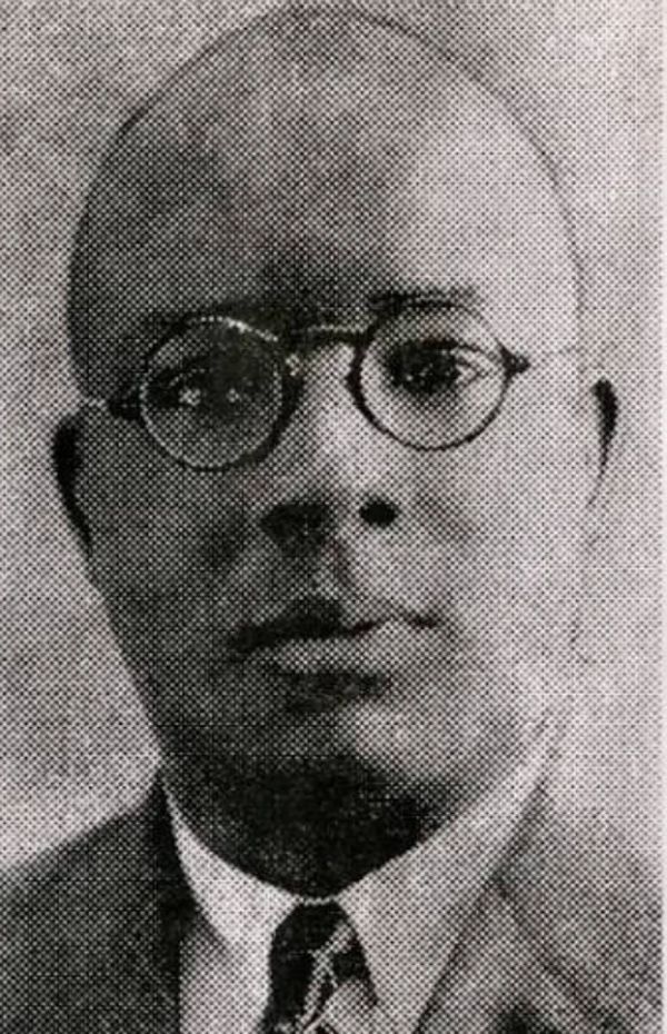 Black and white photo of a bald man wearing glasses and a suit.