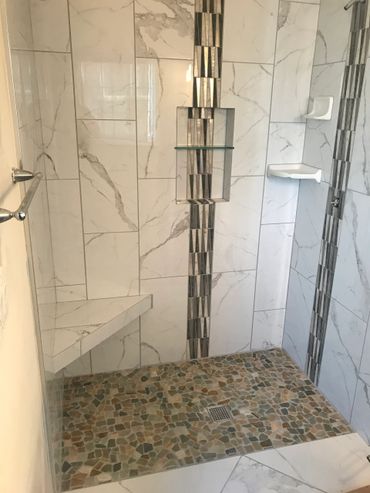 Modern walk-in shower with marble tiles and pebble stone floor.