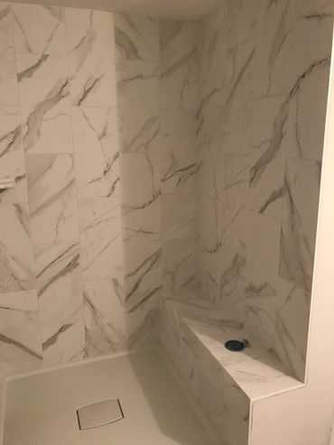 A modern shower with marble-patterned tiles and a built-in bench.