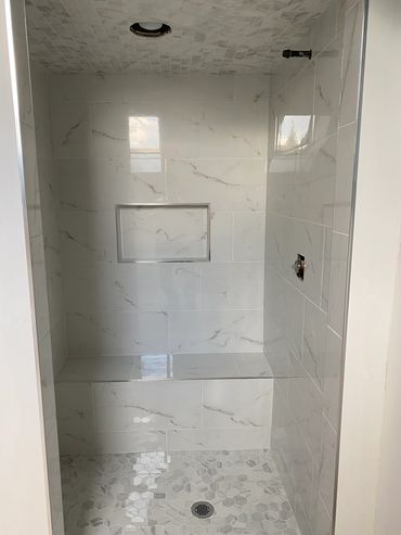Modern shower with marble-style tiles and built-in bench.
