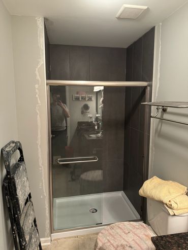 Bathroom shower area under renovation with glass door and dark tiles.