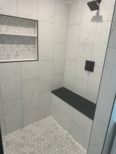 Modern shower with white marble tiles and a black bench.