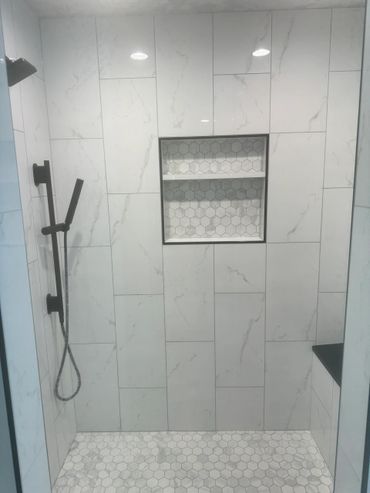 Modern white tiled shower with hexagonal floor and built-in shelf.