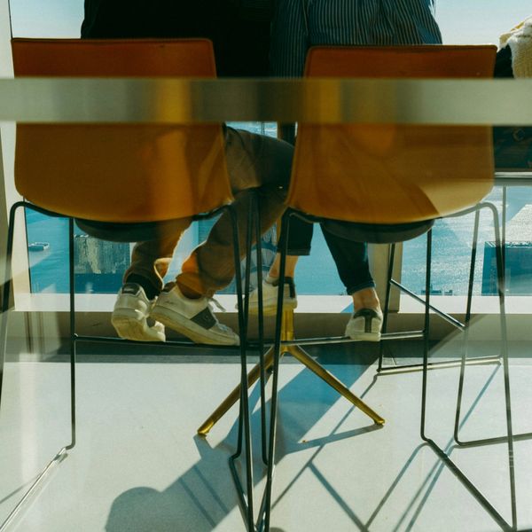 Two people sitting on chairs by a window with a view of water and boats.