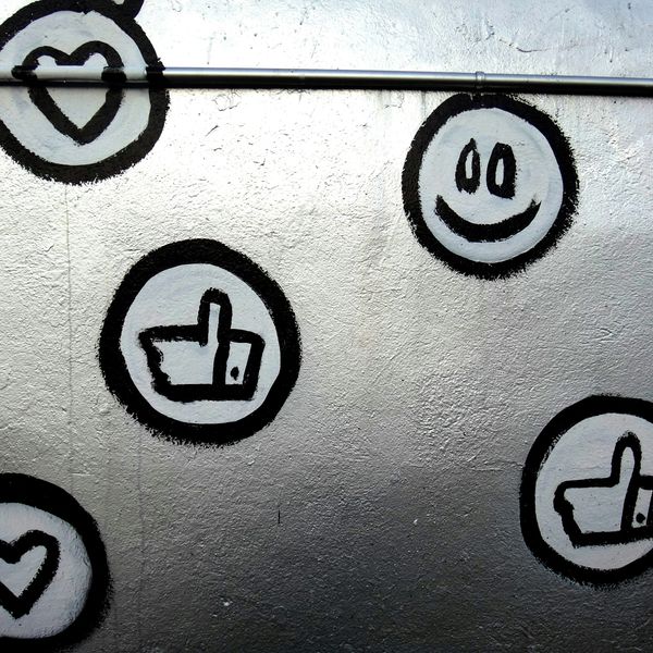 Black and white graffiti of smiley faces, thumbs-up, and hearts on a wall.