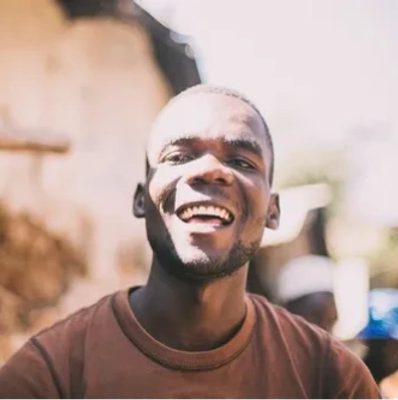 A young man smiling joyfully in natural light.
