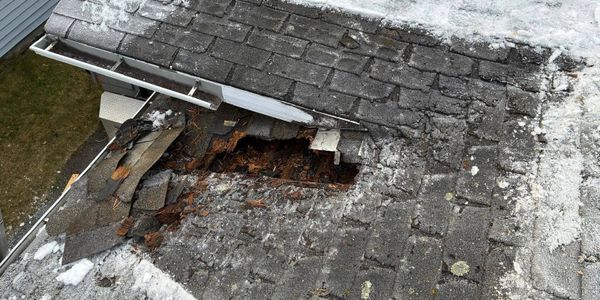 Damaged roof with missing shingles and rotted wood beneath.
