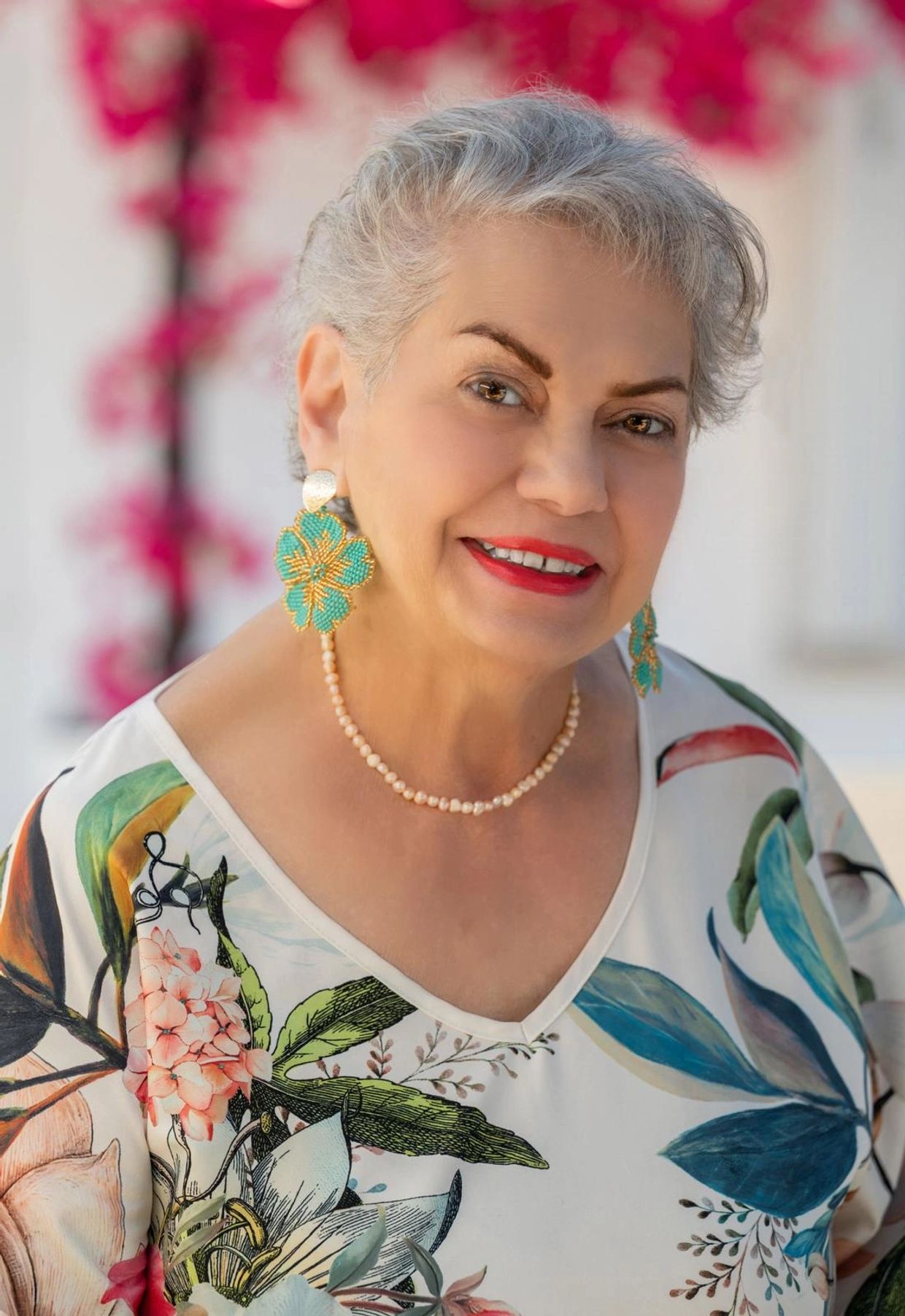 Smiling elderly woman with floral earrings and a colorful blouse.