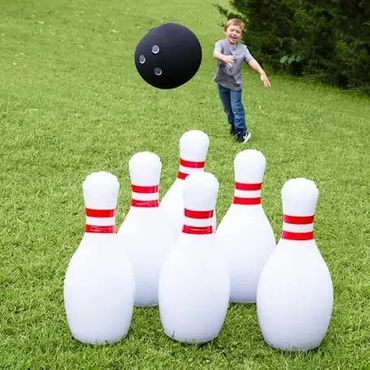 A child playing outdoor bowling with a large ball and pins on grass.