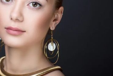 Close-up of a woman wearing large gold hoop earrings and a gold necklace.