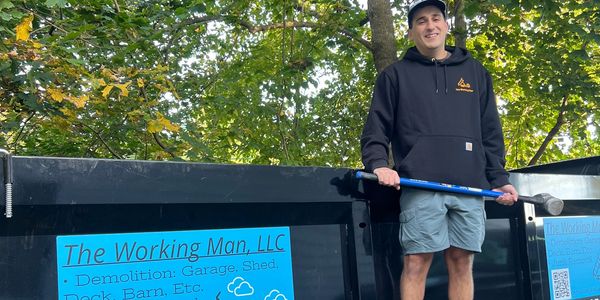 A man stands smiling next to a dumpster with a demolition company sign.